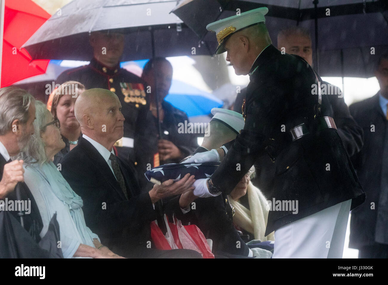 David Glenn, son of former astronaut and U.S. Senator John Glenn receives the folded American flag from the Commandant of the U.S. Marine Corps, General Robert B. Neller, during a graveside interment ceremony at Arlington National Cemetery on Thursday, April 6, 2017 in Virginia. He was the first American to orbit Earth on Feb. 20, 1962, in a five-hour flight aboard the Friendship 7 spacecraft. In 1998, Glenn broke another record by returning to space at the age of 77 on the Space Shuttle Discovery. Photo Credit: (NASA/Aubrey Gemignani) Stock Photo