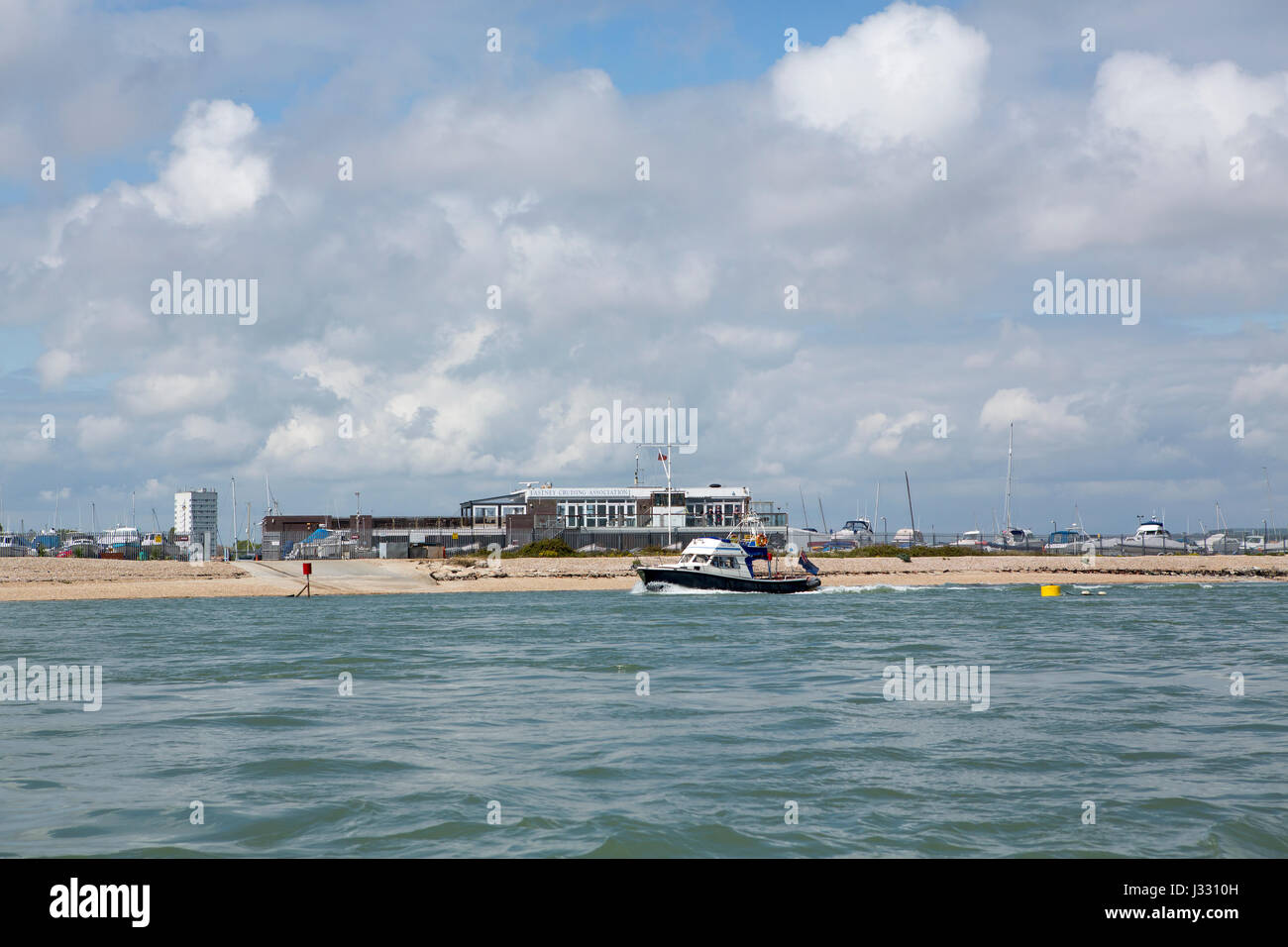 Small motor vessel leaving Langstone harbour passing by the Eastney sailing club. Stock Photo
