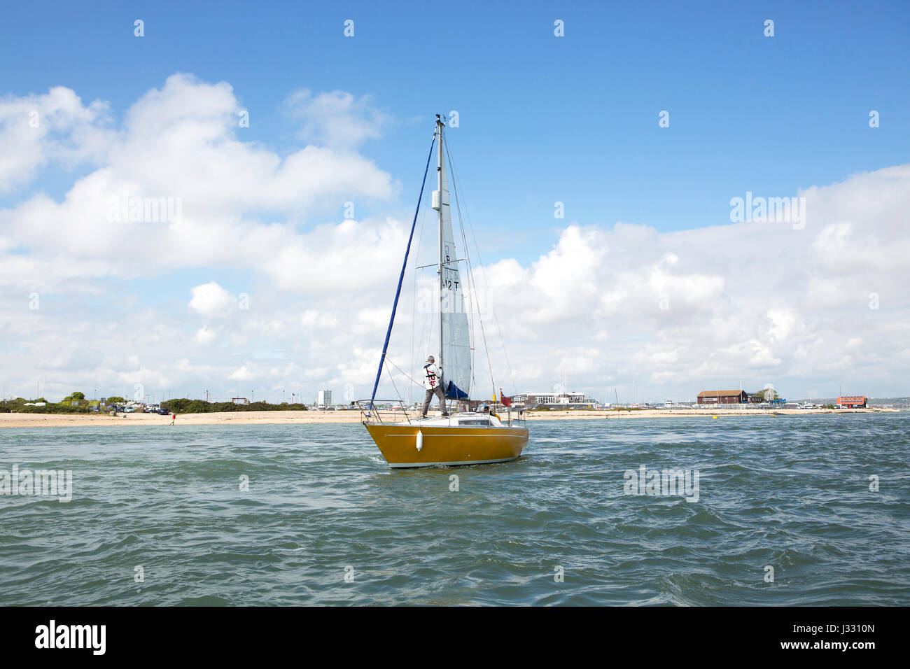 Small yacht leaving Langstone harbour. Person standing on deck trimming the sails. Stock Photo