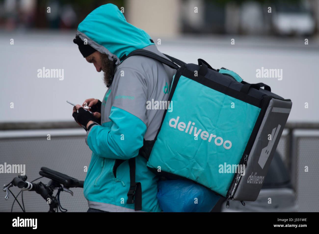 A Deliveroo worker on a bicycle with a Delivroo branded rucksack carrying takeaway food. Stock Photo
