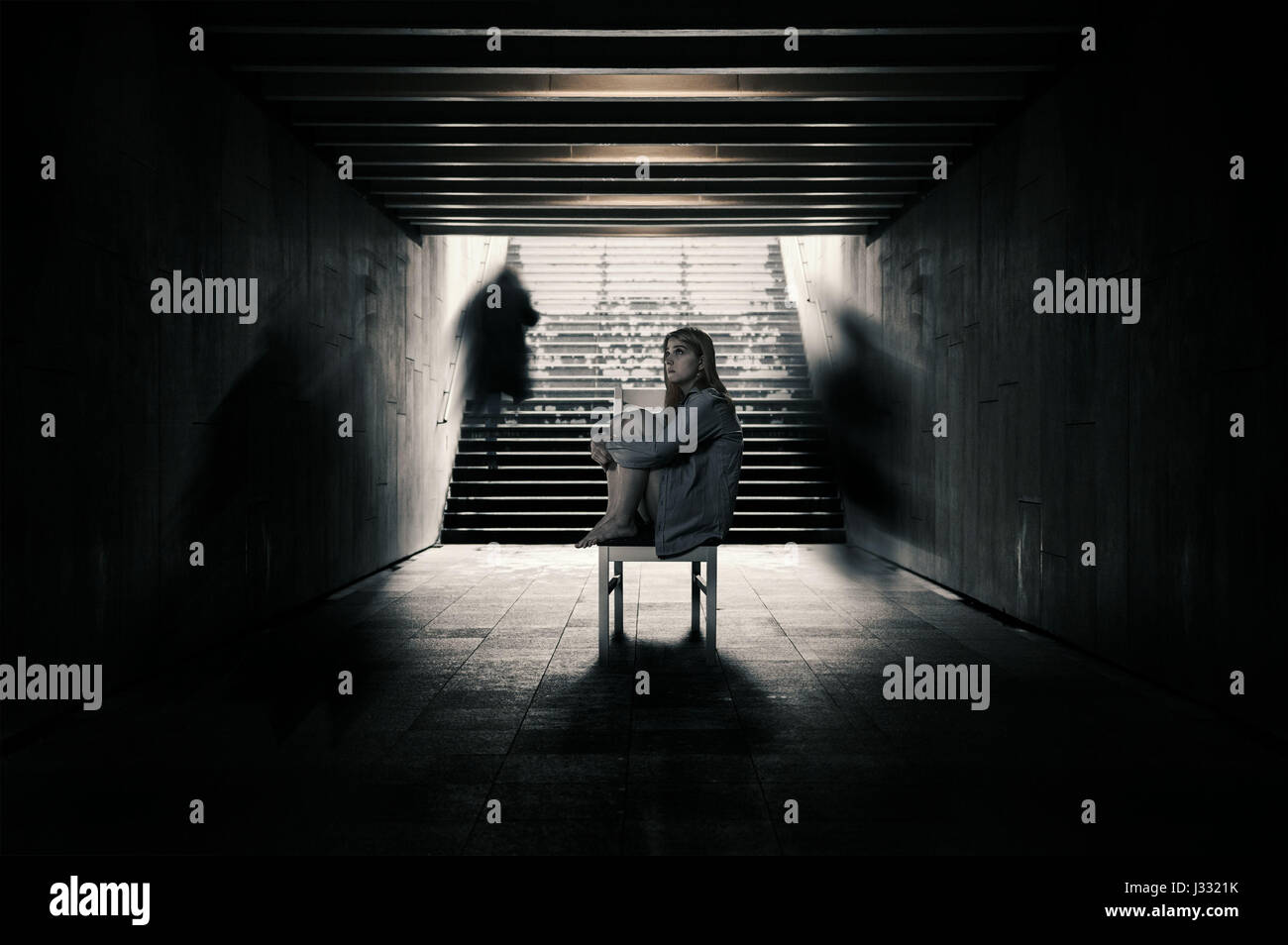 Young woman alone in a tunnel and strangers pass beyond. Conception of loneliness Stock Photo