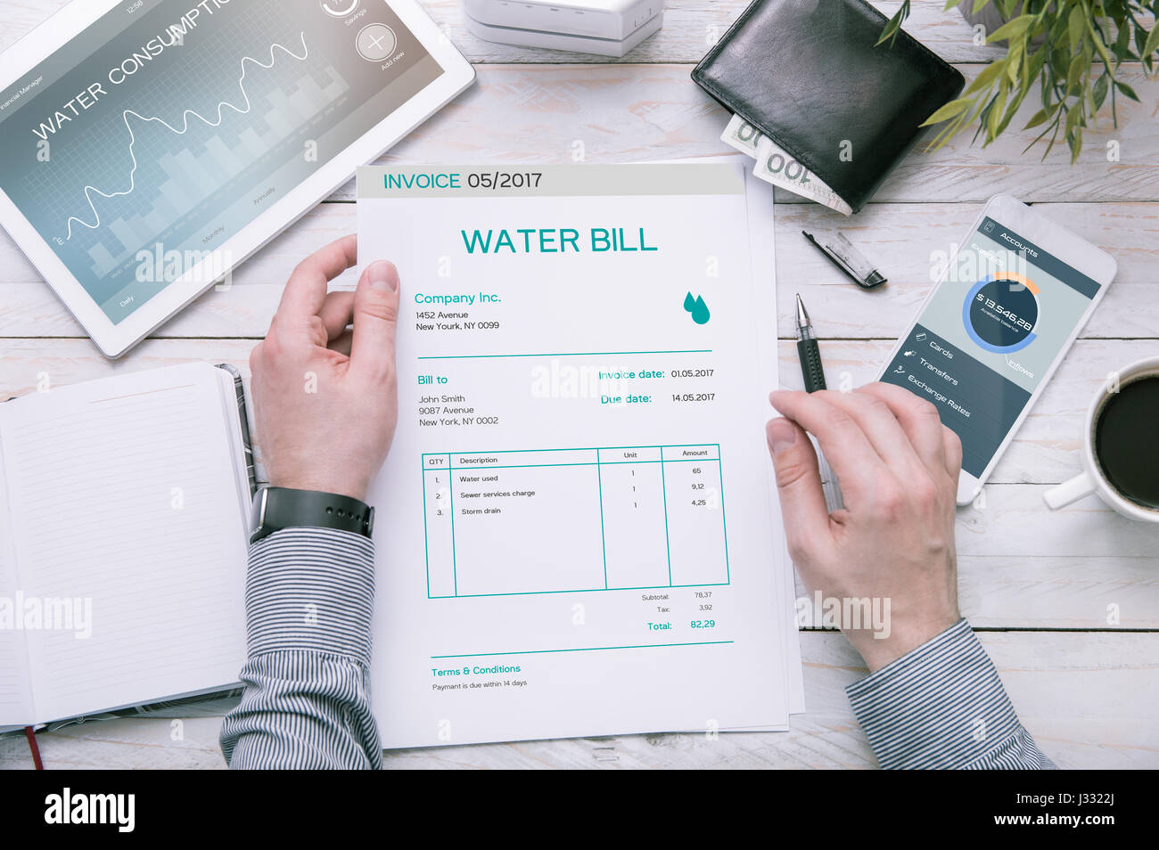 Man holds invoice of water usage over desk with tablet and smartphone with applications made in graphic program. Stock Photo