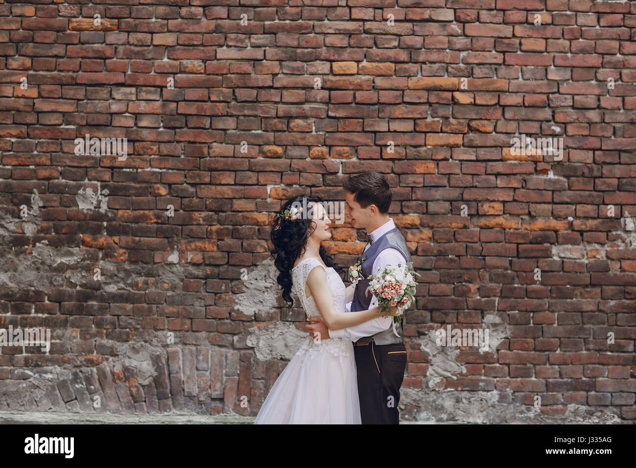 bride and groom standing at a high brick wall Stock Photo - Alamy
