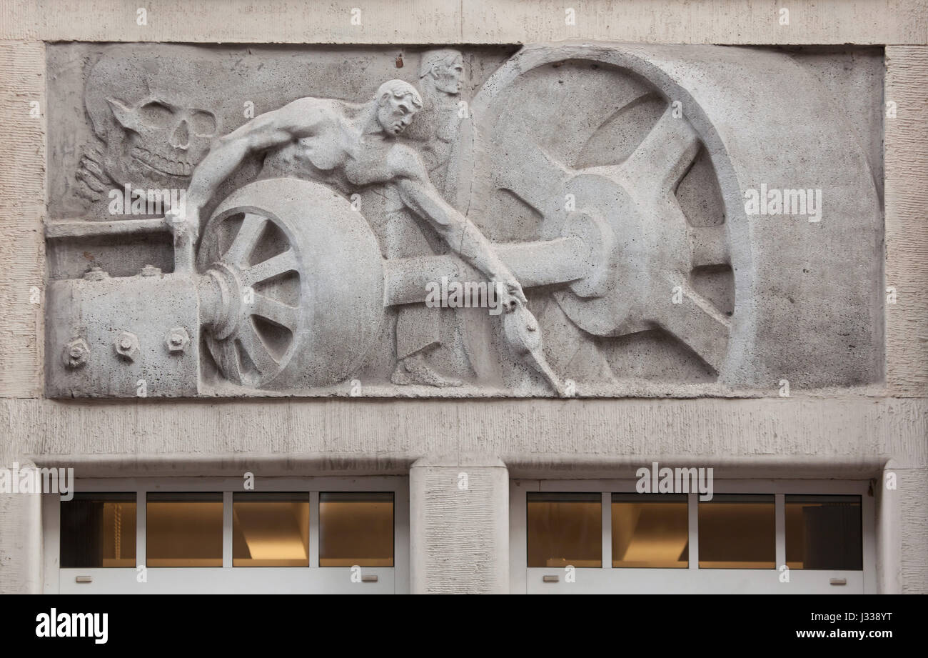 Workers lubricating the machine. Relief by Hungarian sculptor Mihaly Biro on the south wing of the Art Nouveau building of the Budapest Workers Insurance Fund in Budapest, Hungary. The building, now used as the seat of the National Social Insurance Centre (OTI), was designed by Hungarian architects Marcell Komor and Dezso Jakab and built in 1913. The north wing was added in the 1930s. Stock Photo