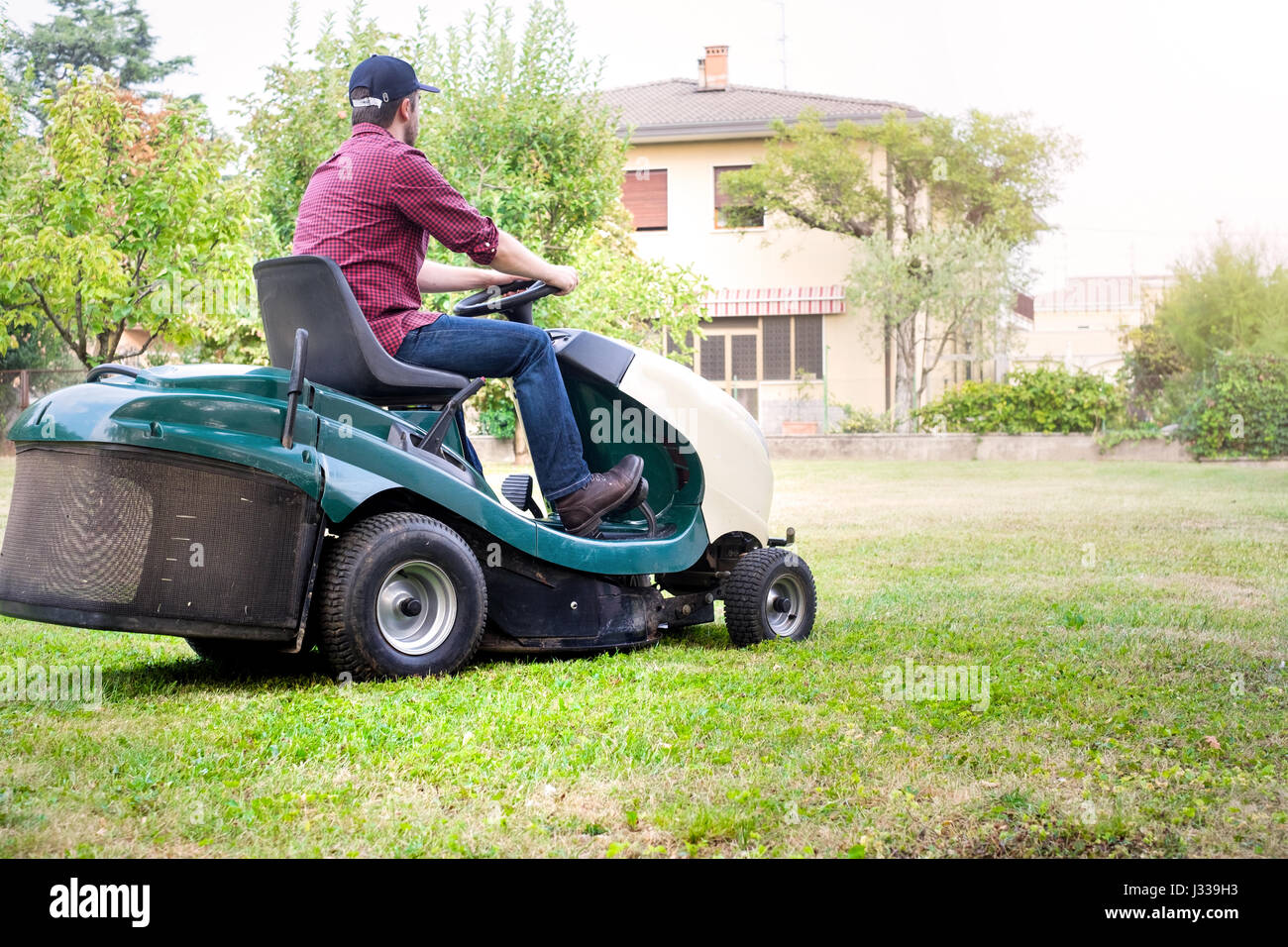 Gardener cutting the grass of a garden seated on a lawn mower Stock Photo