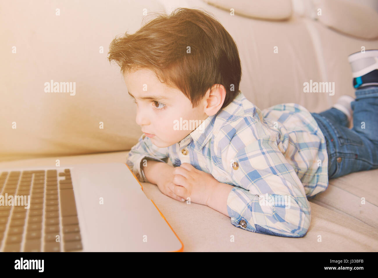 Little boy lying on the couch while looking at a laptop Stock Photo - Alamy