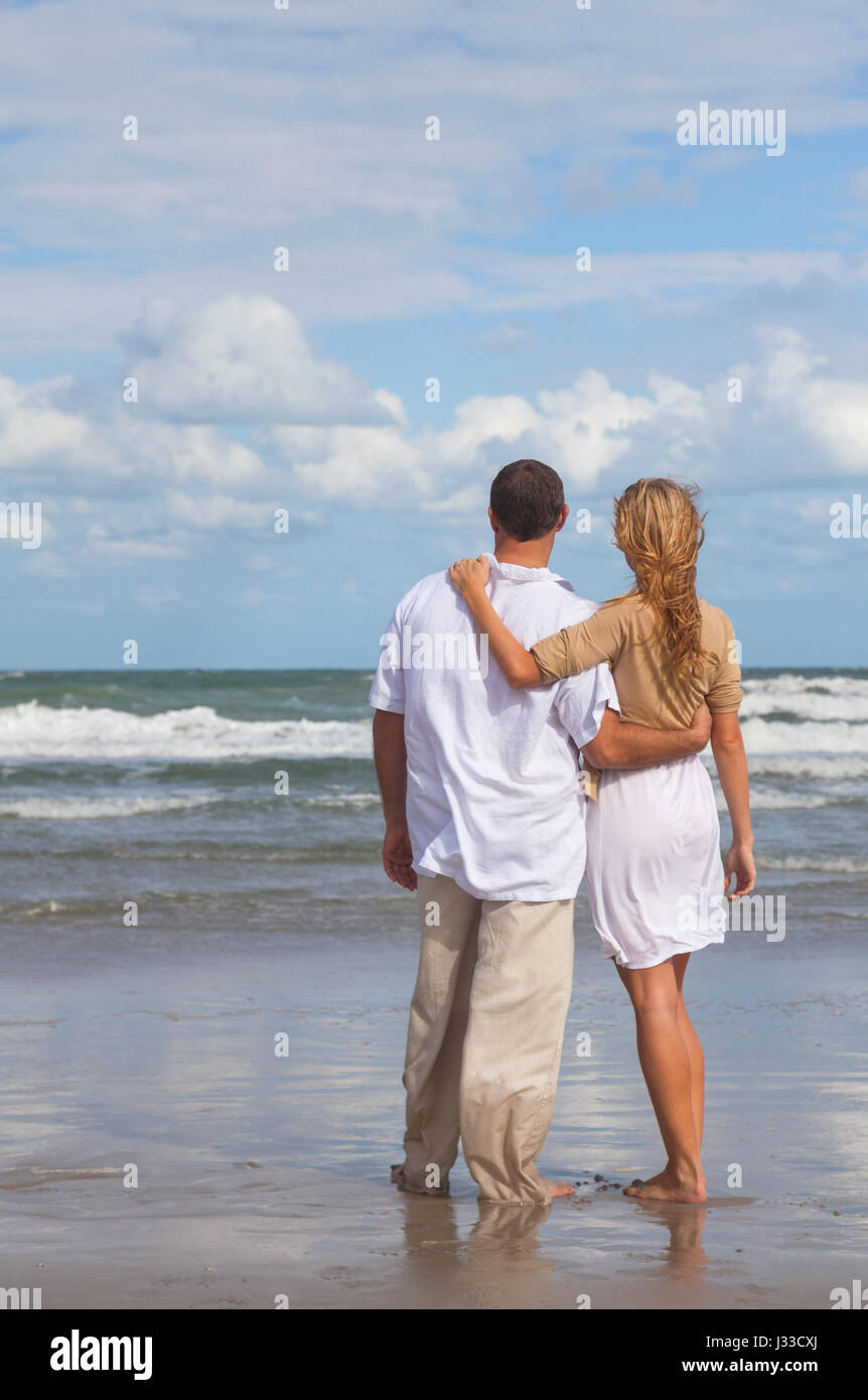 Rear view of romantic young man and woman couple embracing on a beach ...