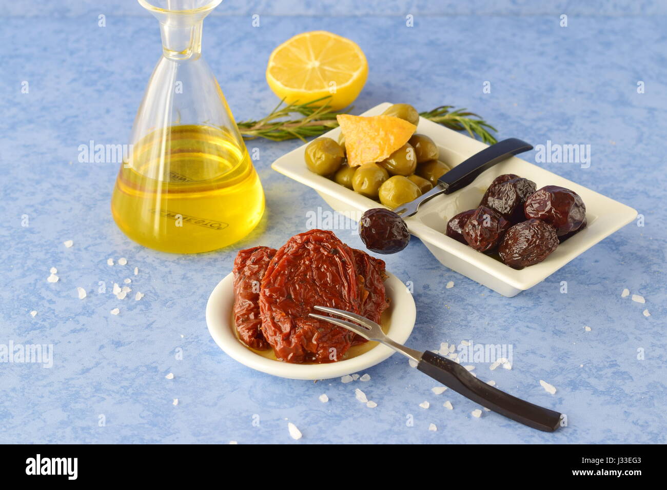 A set of dishes of greek cuisine: olives, sun dried tomatoes, lemon, glass jar with olive oil. Traditional Greek food. Mediterranean lifestyle Stock Photo