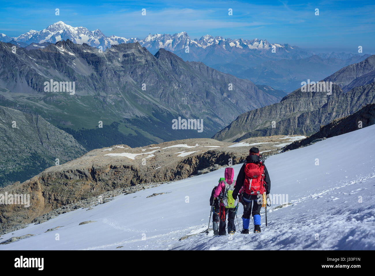 Several persons descending on glacier from Gran Paradiso, Mont Blanc in background, Gran Paradiso, Gran Paradiso Nationalpark, Graian Alps range, valley of Aosta, Aosta, Italy Stock Photo