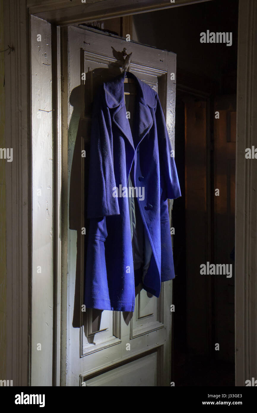 Old, dark blue coat hanging on a door in moonlight Stock Photo