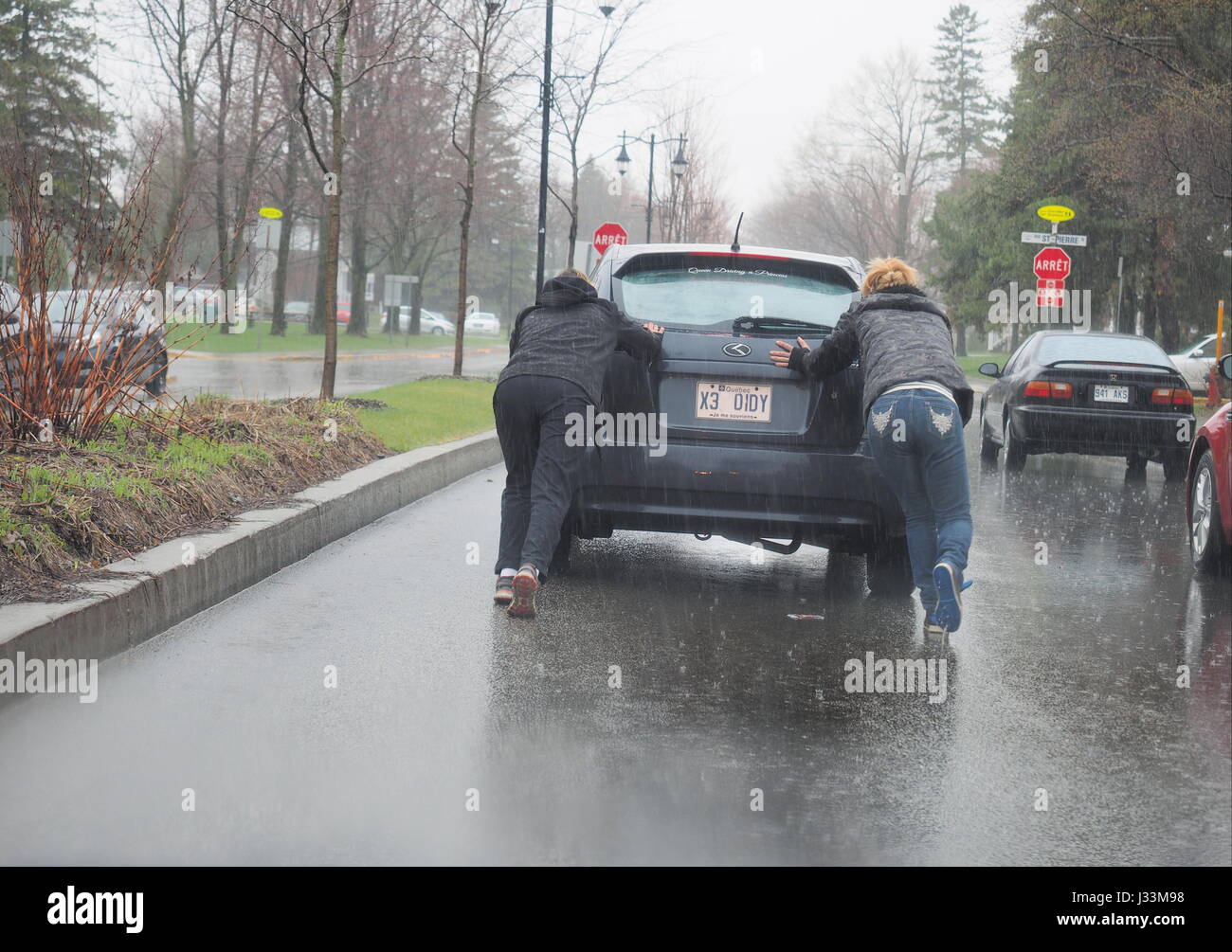 Two women pushing a car in the rain. Stock Photo