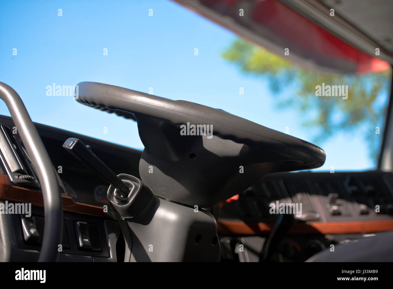Modern cabin of semi truck with the steering wheel, column, dashboard, control levers on the background of the windshield through which you can see Stock Photo