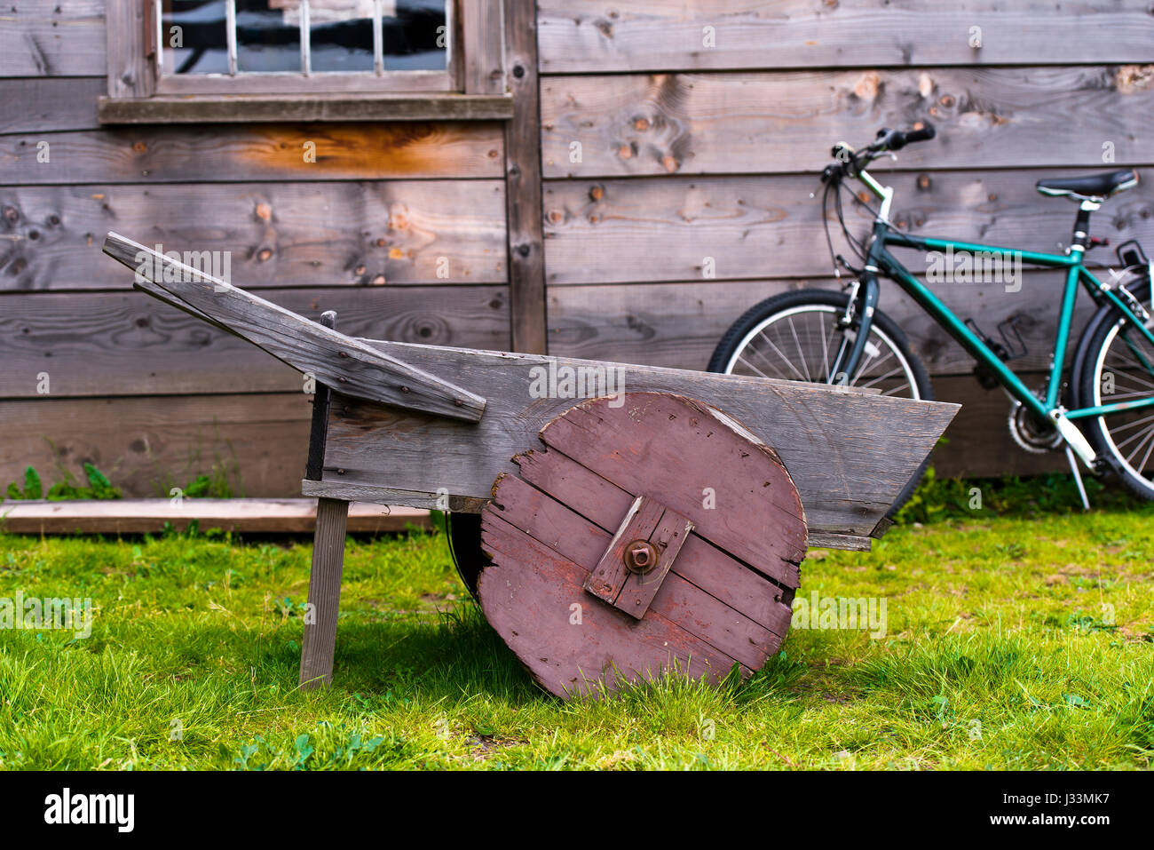 Old wooden wheelbarrow with wooden wheel represents the past and modern design of the bike with green frame standing in old wooden barn Stock Photo
