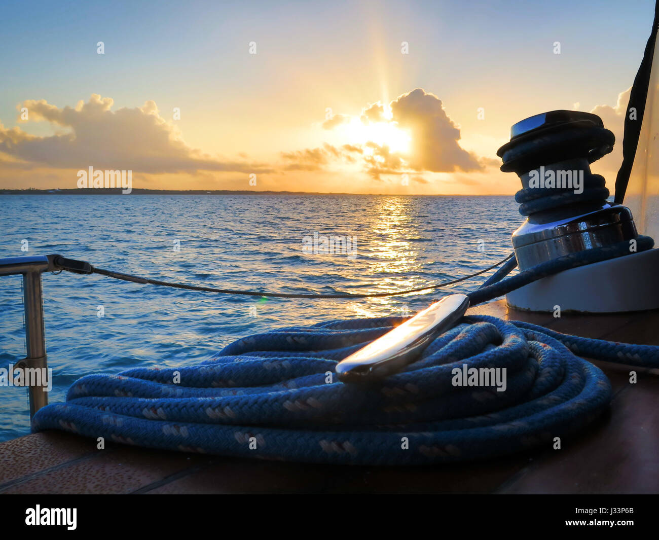 Detail of winch, cable and cleat in a sailboat during sunset. Stock Photo