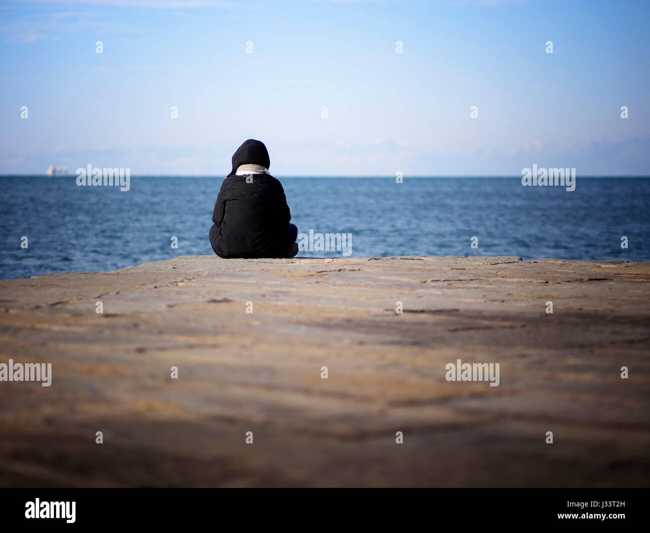 One person seated at the end of a pier enjoying the sea in a cold morning. Stock Photo