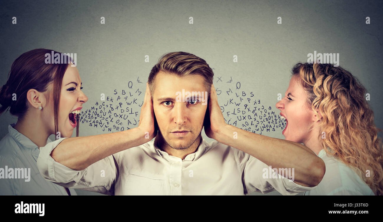 Two young women screaming at a calm man covering his ears with hands ignoring them. Anger management emotional intelligence concept. Love triangle. Ne Stock Photo