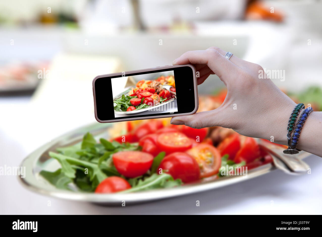 Woman holding a phone and photographed salad of red tomato Stock Photo