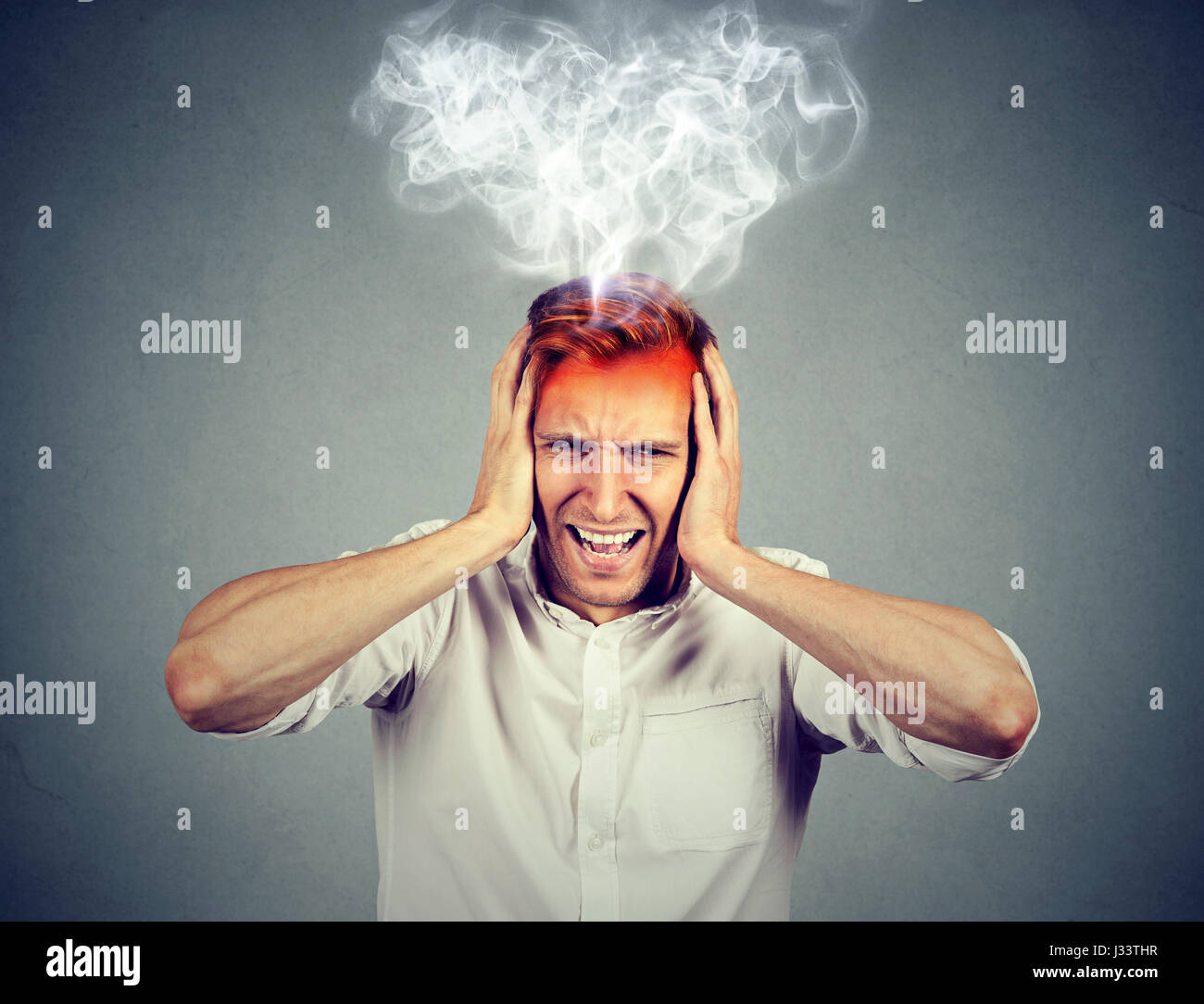 Portrait young stressed man screaming frustrated overwhelmed steam coming out up of head isolated on grey wall background. Negative human face express Stock Photo