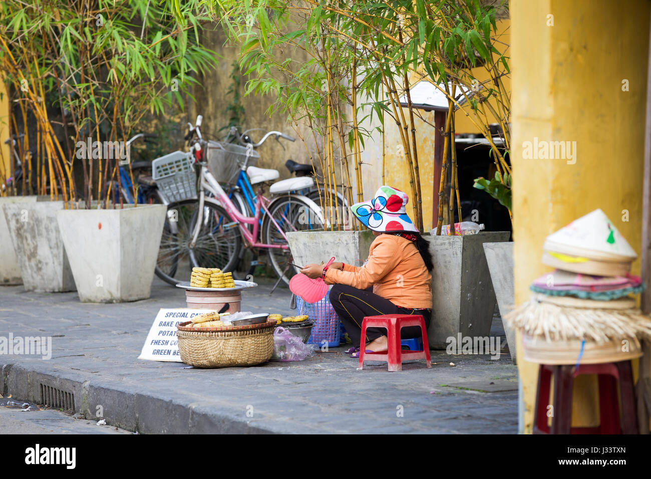 HOI AN, VIETNAM - MARCH 13: Vietnamese woman selling food on the street of Hoi An Ancient Town, UNESCO World Heritage Site on March 13, 2014 in Hoi An Stock Photo