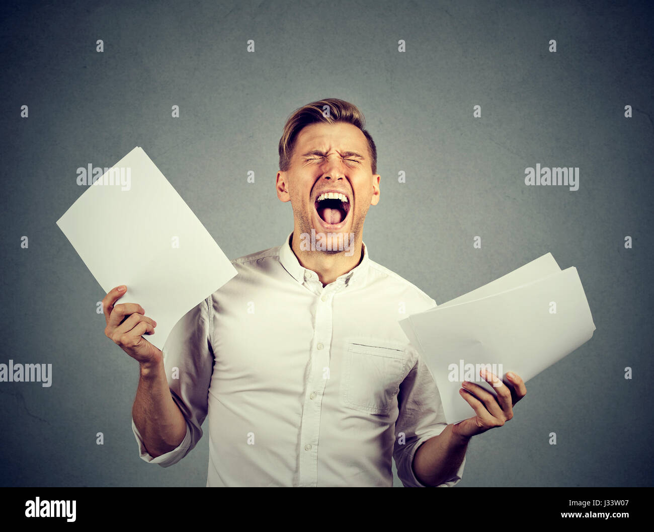 Angry stressed screaming business man with documents papers paperwork isolated on gray wall background. Negative emotions face expression Stock Photo