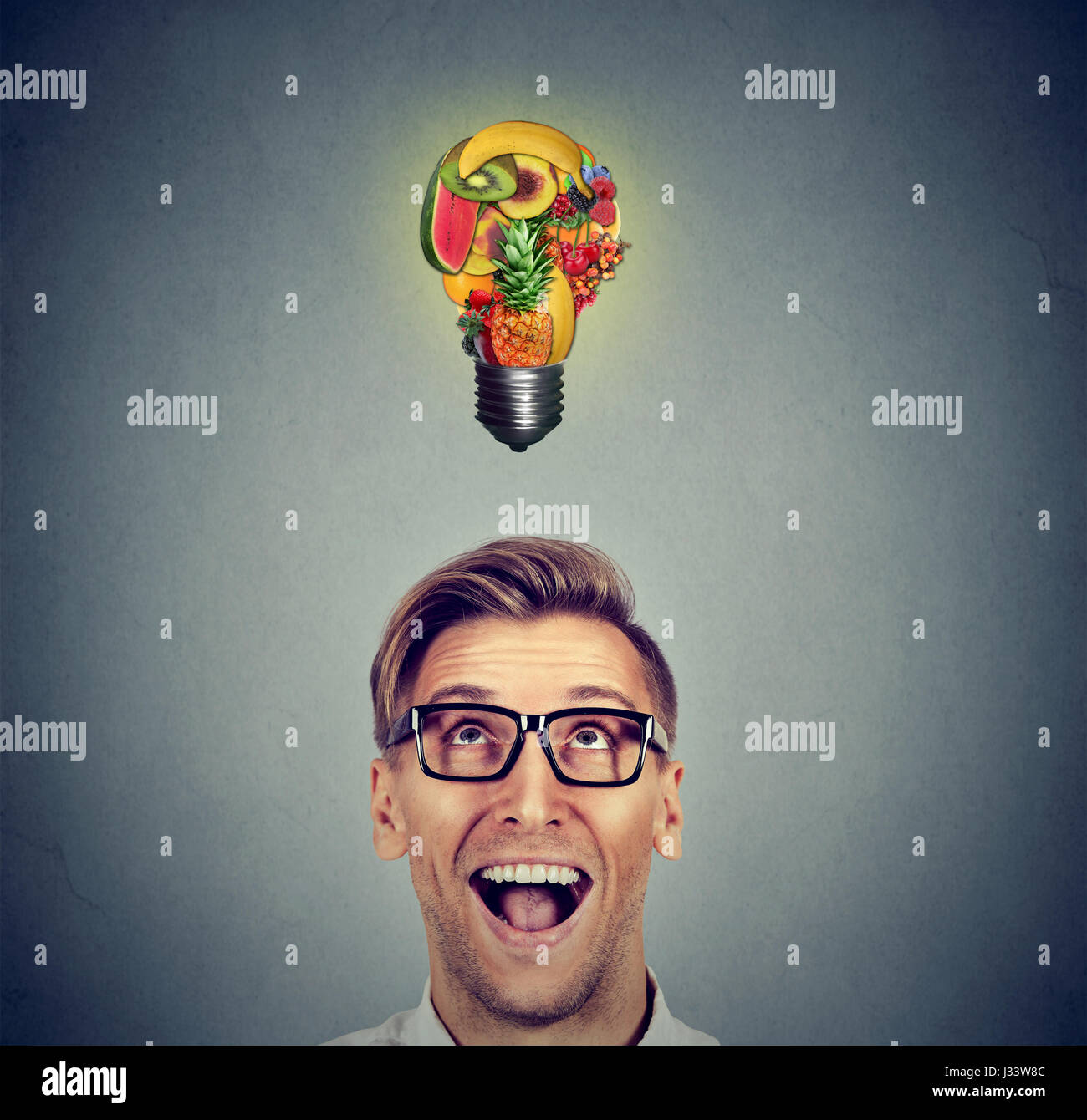 Eating healthy idea and diet tips concept. Portrait headshot man looking up light bulb made of fruits above head on gray wall background. Stock Photo
