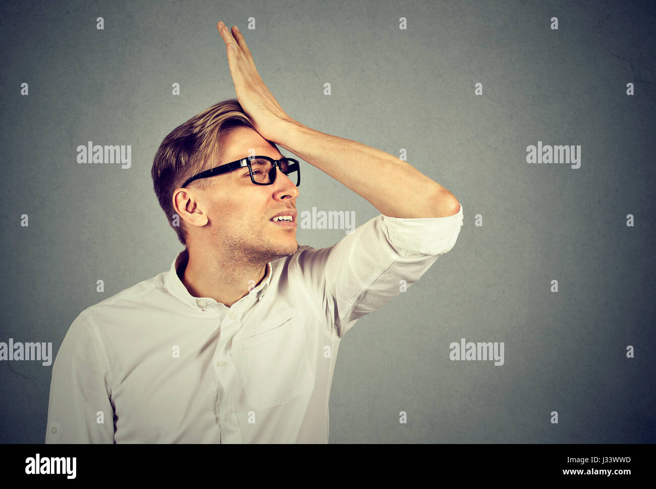 Regrets wrong doing. Silly young man in glasses slapping hand on head having a duh moment. Negative human emotion facial expression feeling, reaction Stock Photo