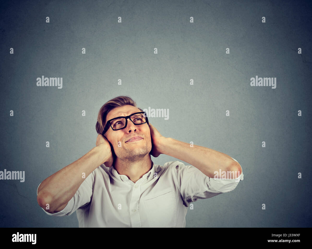 young annoyed, unhappy, stressed man covering his ears, looking up
