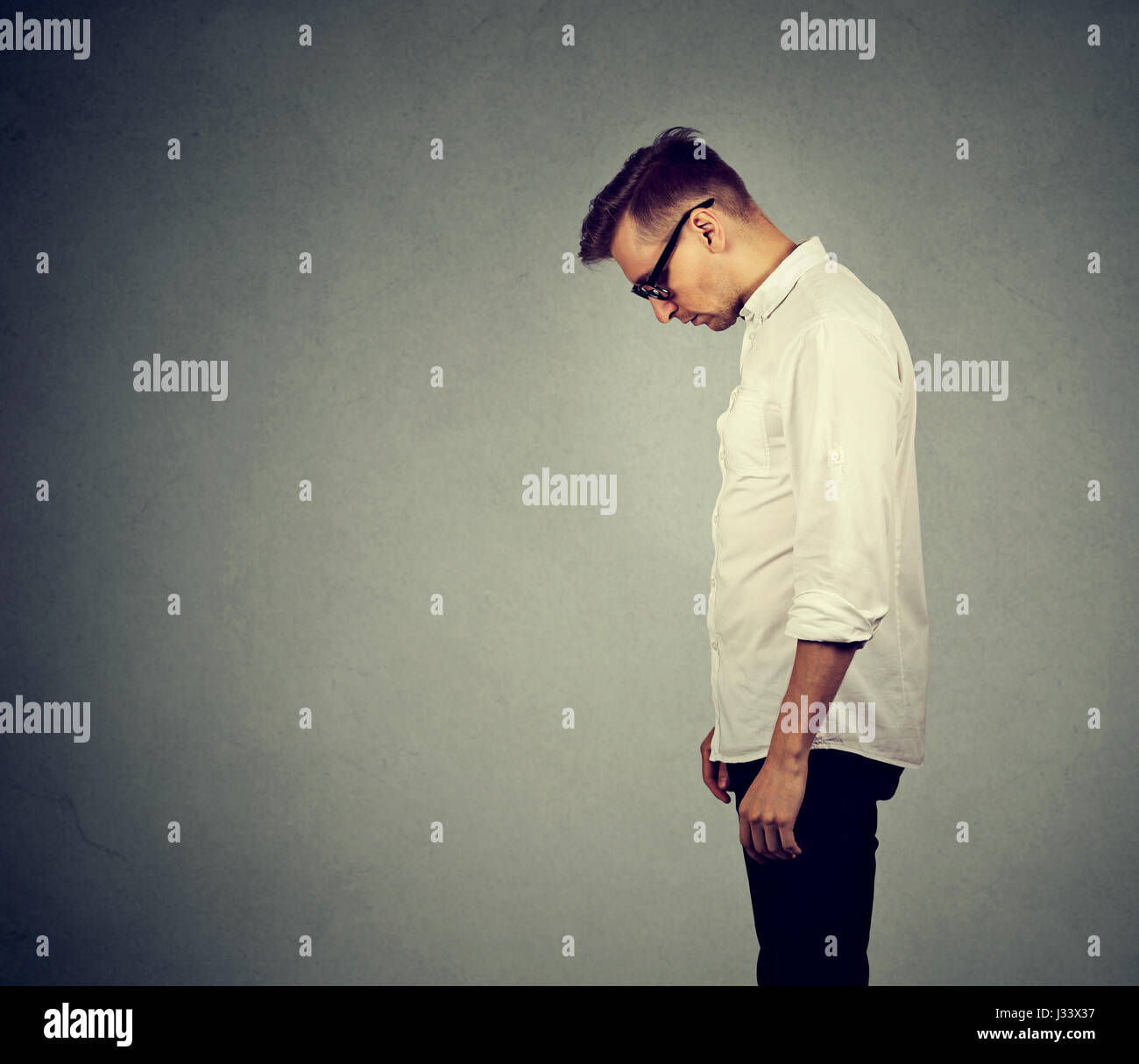 Side profile sad lonely young man looking down has no energy motivation in life depressed isolated on gray wall background Stock Photo