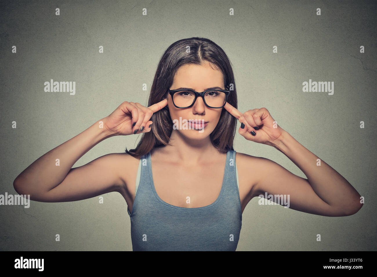 Portrait young angry unhappy woman with glasses plugging ears with fingers looking at you annoyed loud noise giving her headache ignoring isolated gra Stock Photo