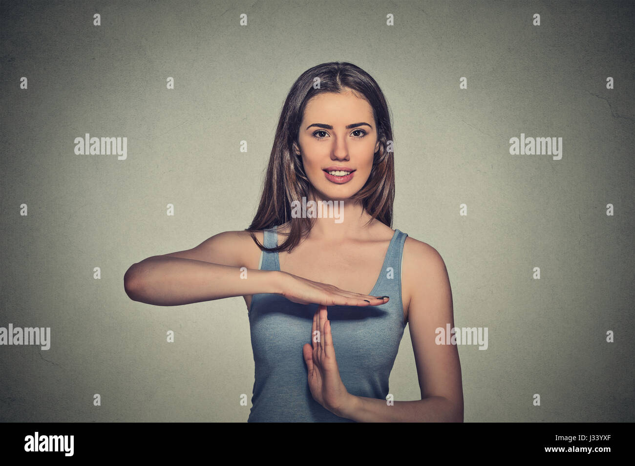 Closeup portrait, young, happy, smiling woman showing time out gesture with hands isolated on gray wall background. Positive human emotion facial expr Stock Photo