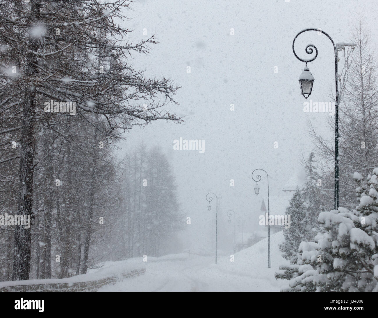 snow snowing falling on a road street scene in the French Alpes with ornate lamp post posts Stock Photo