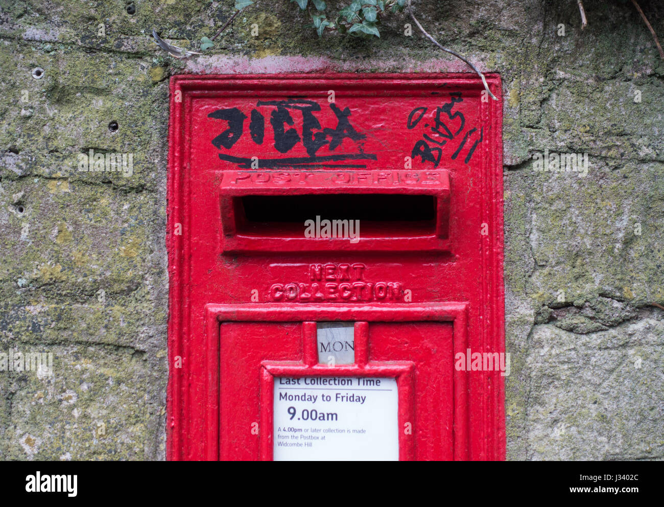 a view of black graffiti on a pill post letter box in a stone wall Stock Photo