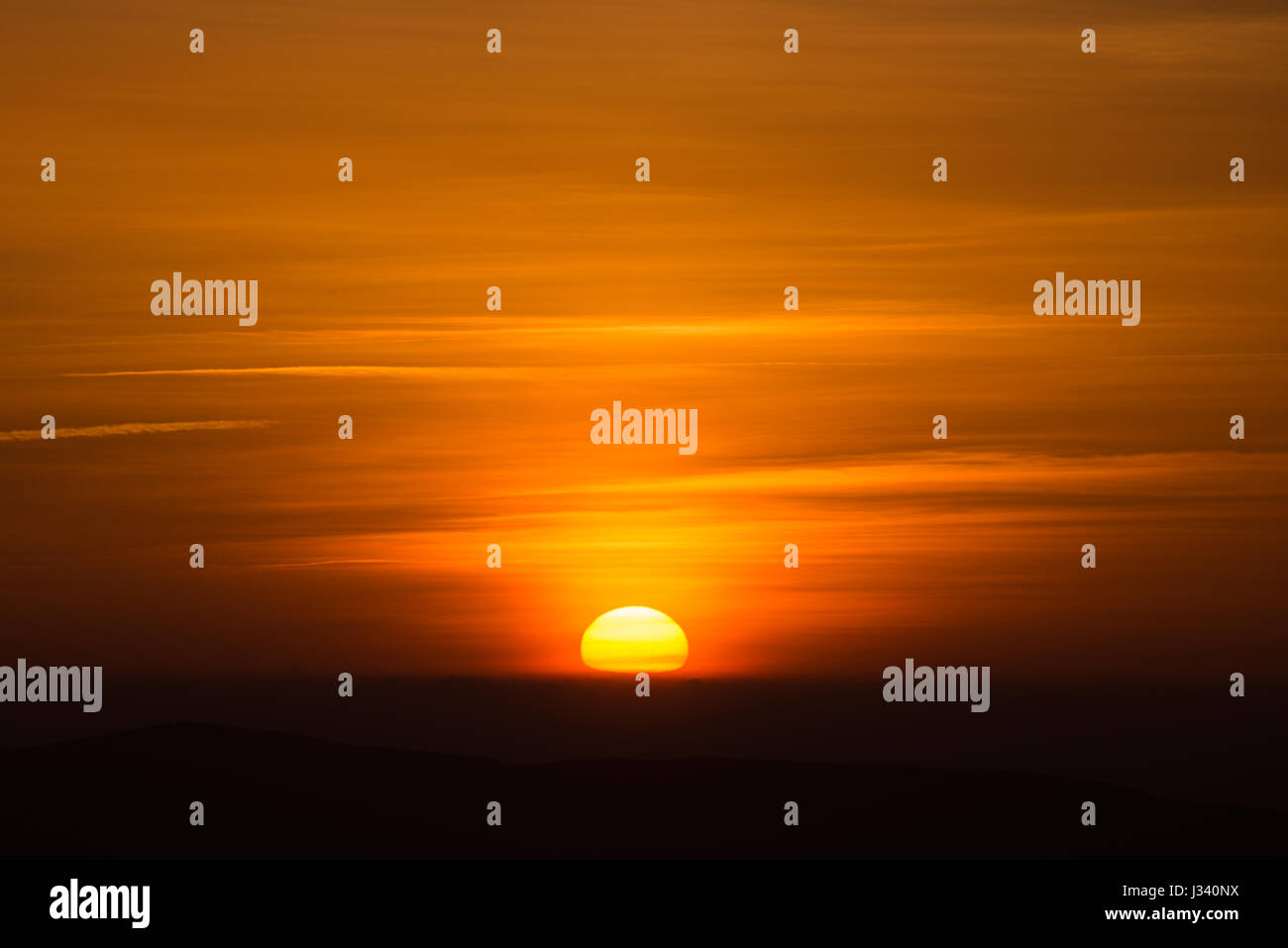 The great orange sphere of the sun sinks behind the horizon Stock Photo