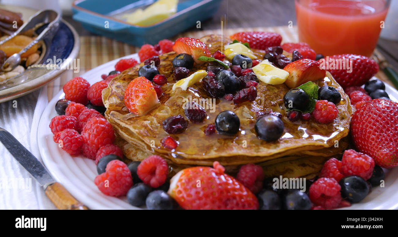 Pouring maple syrup over a breakfast of pancakes with berries and dry