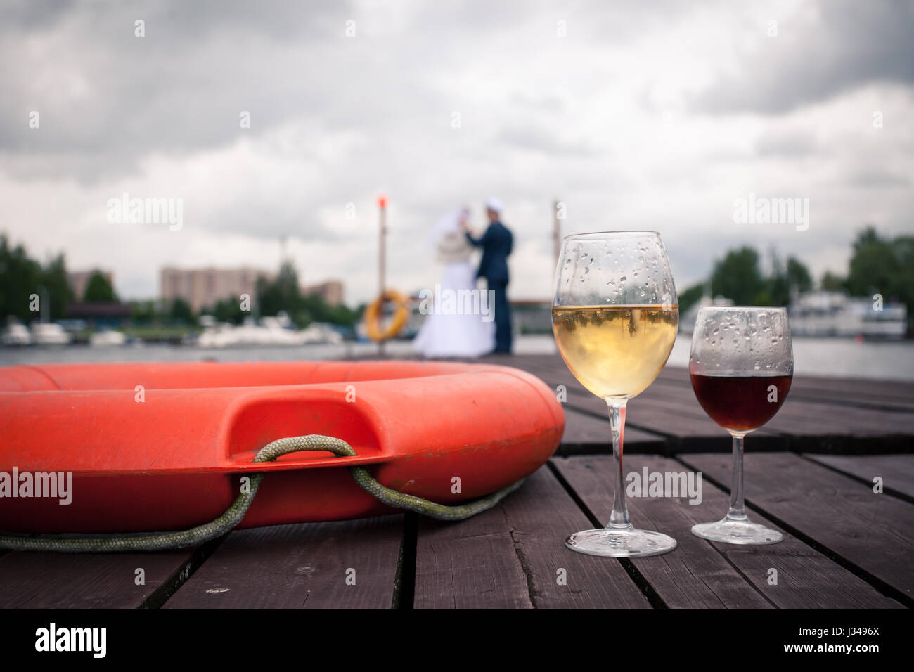 The glasses of wine on the pier next to a life raft amid honeymooners, romantic evening Stock Photo