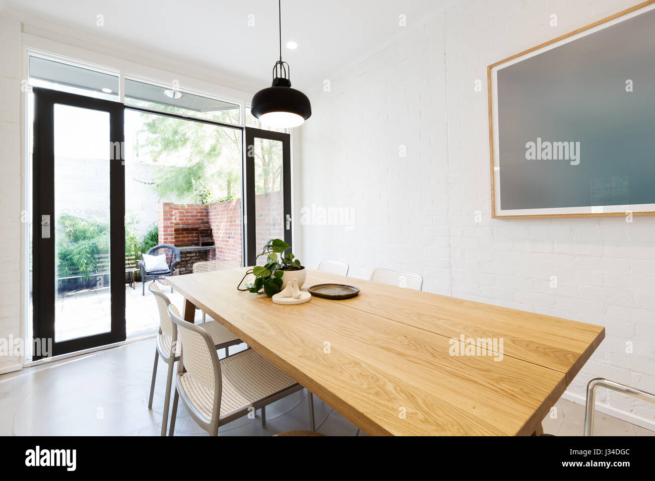 Scandi styled dining room interior with outlook to courtyard through open french doors Stock Photo