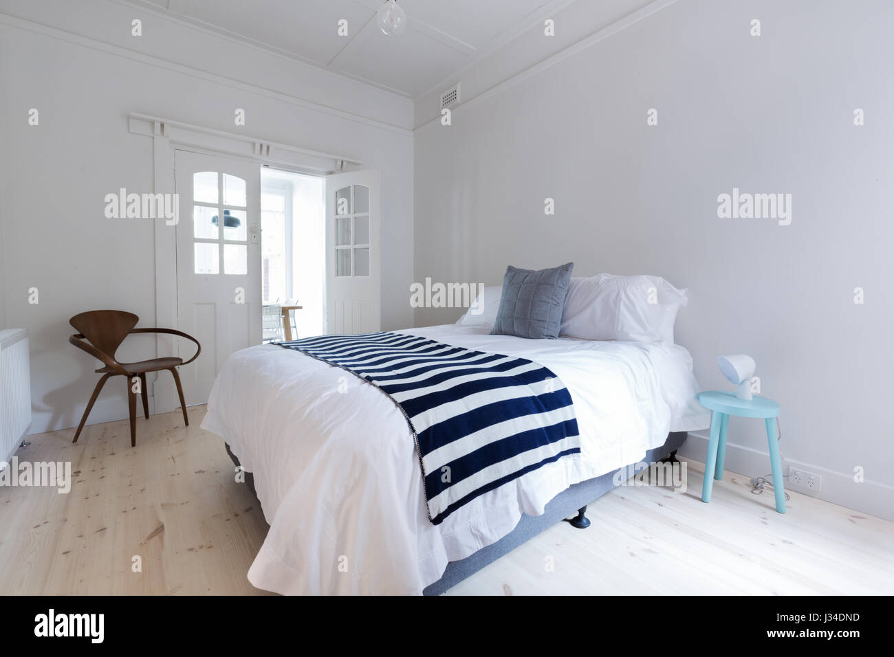 Crisp white Danish stylish bedroom with striped throw rug and blue side table Stock Photo