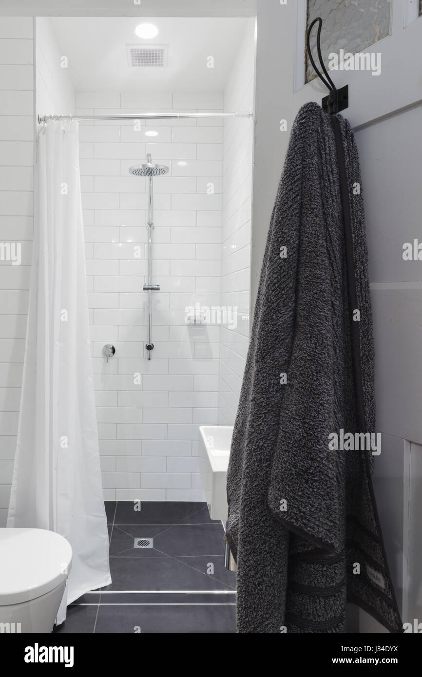 Small white tiled ensuite bathroom with shower and toilet and hanging towel on a hook Stock Photo