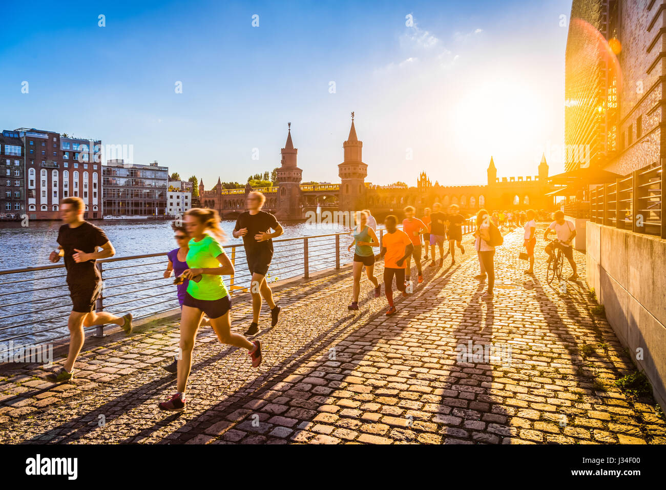 Group of female and male young runners jogging outside in golden evening light at sunset in summer with retro vintage style toned filter effect Stock Photo