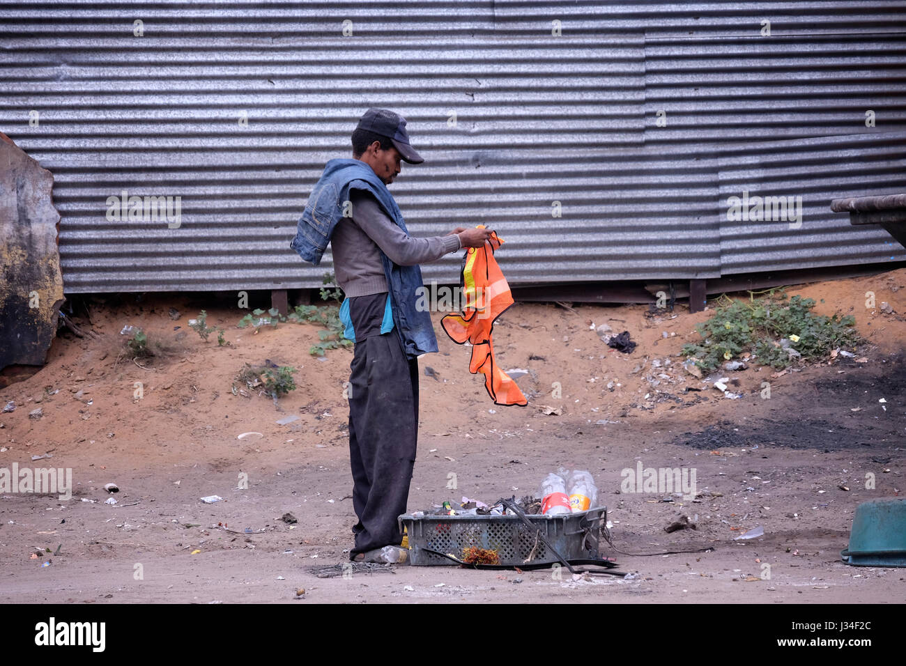 A man rummaging through garbage bin in the street in Maputo, the