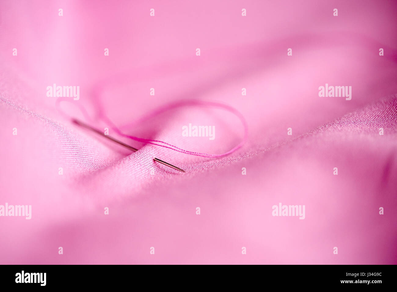 sewing needle with thread stuck into pink fabric Stock Photo Alamy