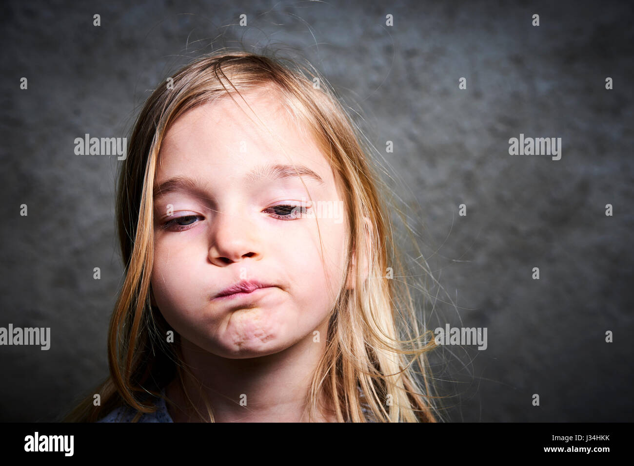 little child blond girl making faces with gray grunge wall background Stock Photo