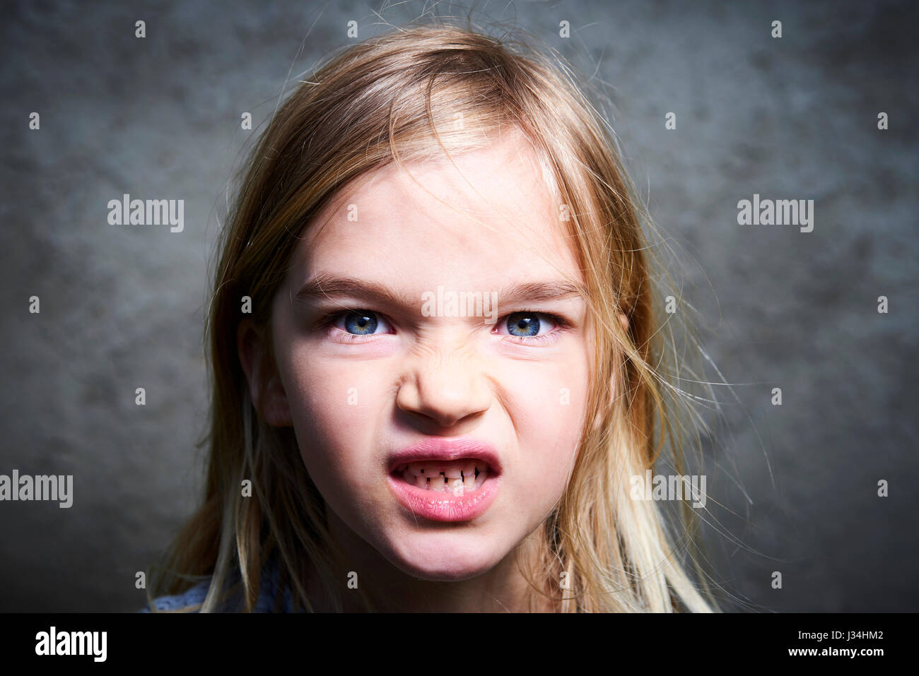 Portrait of child little blond angry girl with gray wall background. Stock Photo