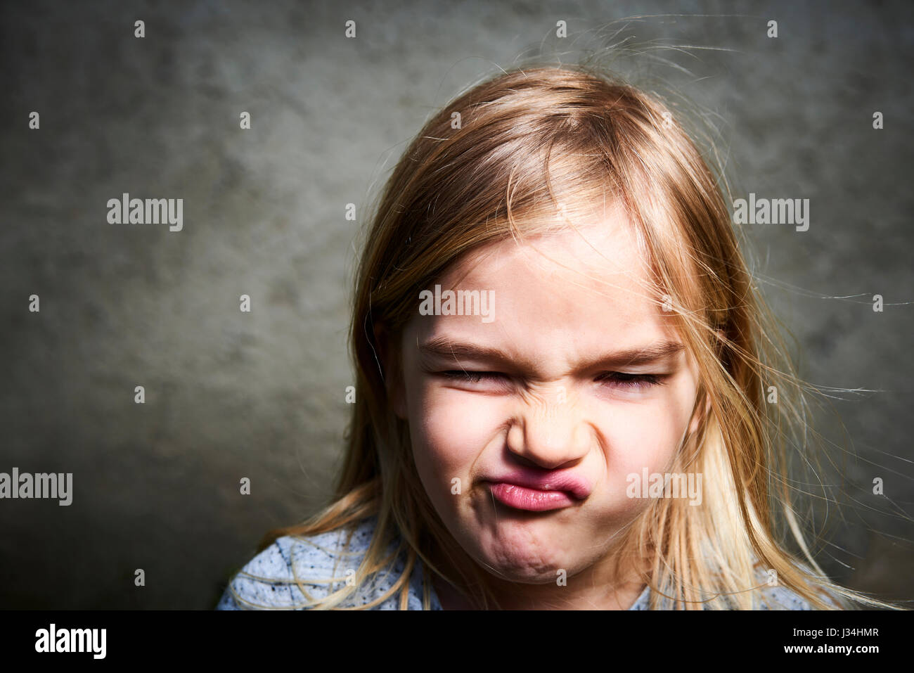 Portrait of child little blond angry girl with gray wall background. Stock Photo