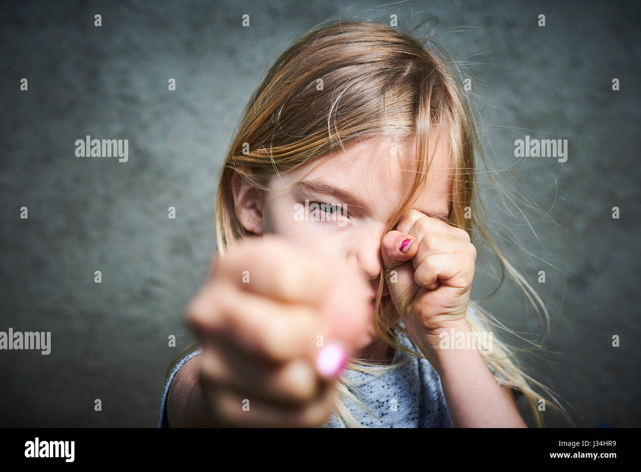 Portrait of child little blond angry girl with gray wall background. Stock Photo
