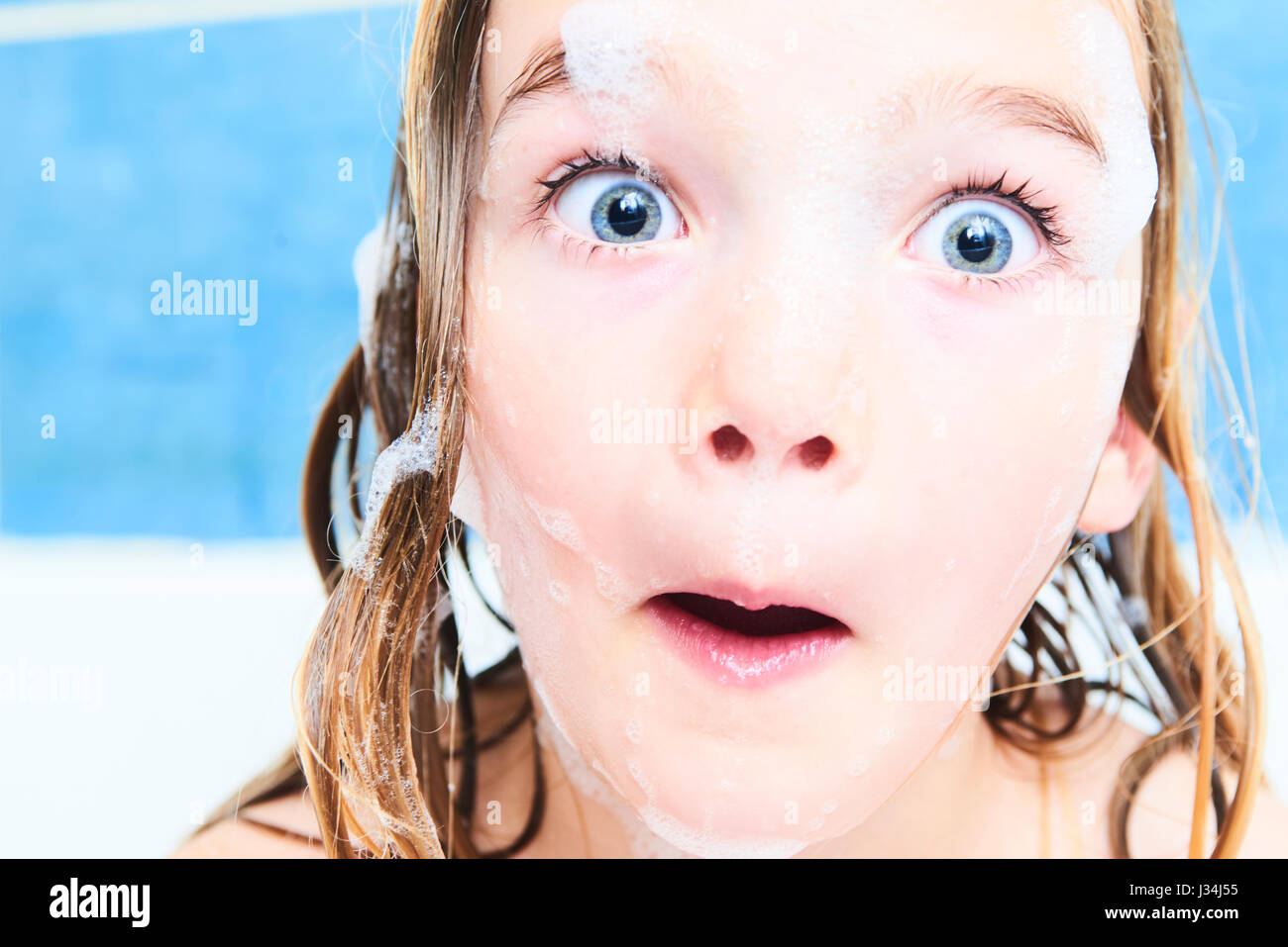 Little blond girl with wet long hair takes a bubble bath, play and have