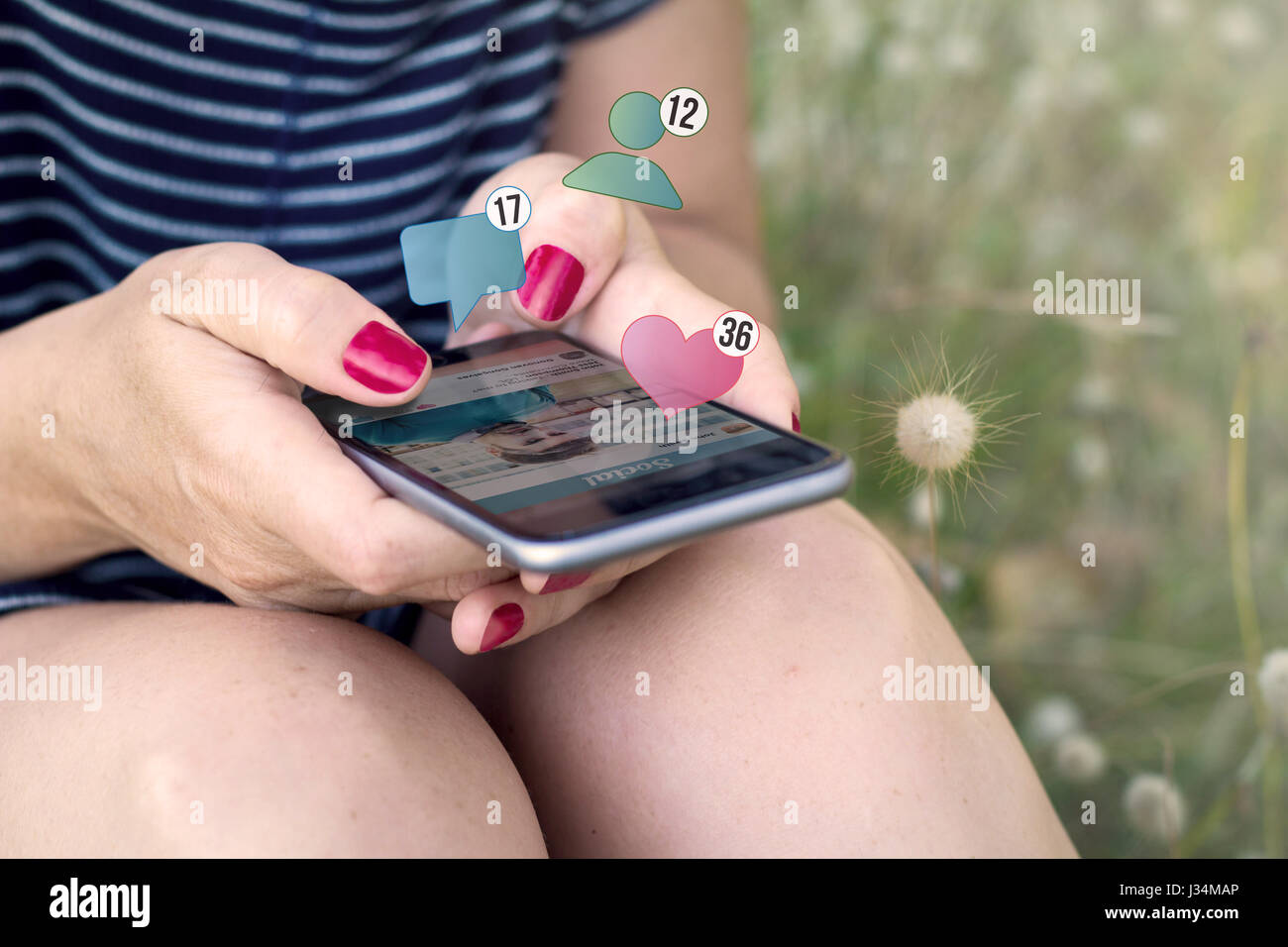 sitting woman checking social stats smartphone on the grass. All screen graphics are made up. Stock Photo