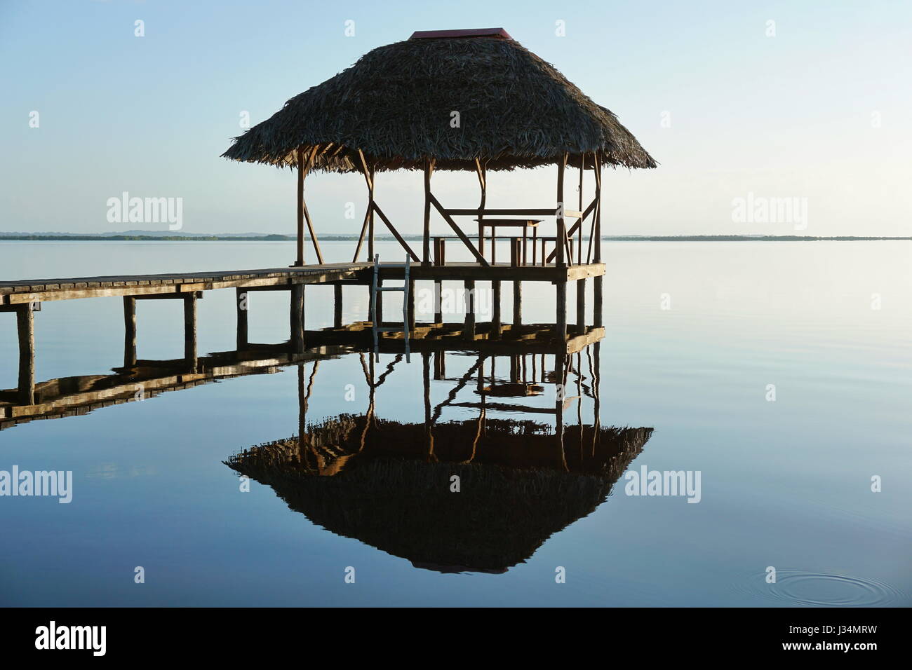 Thatched hut overwater and its reflection on a calm water surface, sunrise light, natural scene, Caribbean sea, Panama, Central America Stock Photo