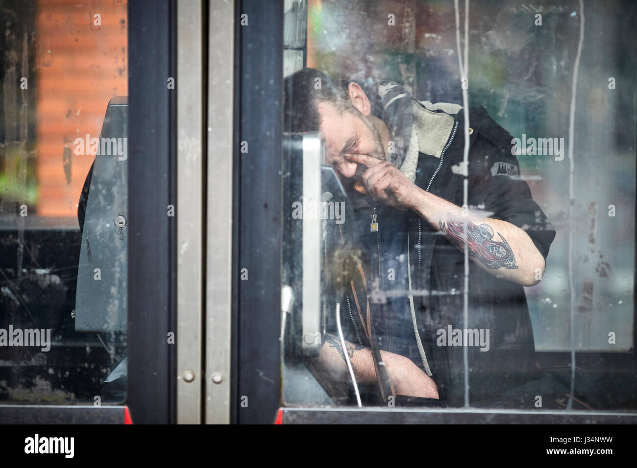 Manchester city centre a man asleep in a public phone box possibly after taking Spice Stock Photo