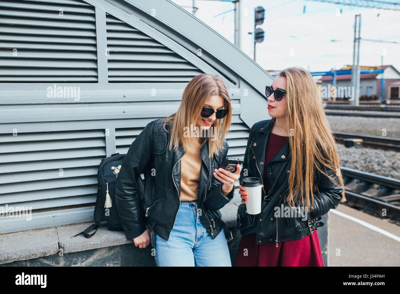 Two Women Talking in the City.Outdoor lifestyle portrait of two best friends hipster girls wearing stylish Leather Jacket and sunglasses with cofee, going crazy and having great time together Stock Photo